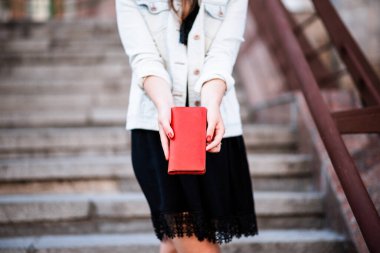 Kırmızı ceketli bir kadın güneşli bir yaz gününde şehirde yürüyüş yapıyor.