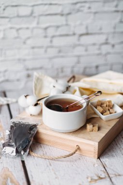 Tahta tepside siyah çay ve metal çaydanlık, şeffaf taklit çay poşeti, beyaz kasede kamış şekeri, açık tahta arka plan, sarı peçete, çay partisi