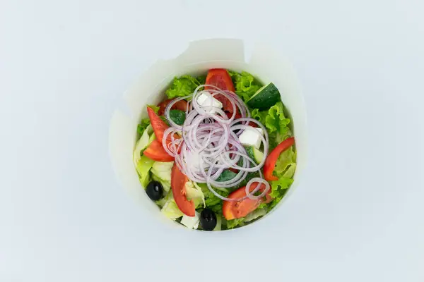 Beyaz arka planda plastik bir kutuda sebze salatası.