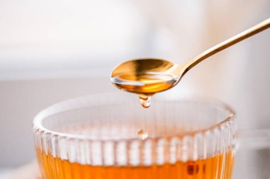 a drop of black tea falls from a golden spoon, macro, close-up view, golden tea, stem composition