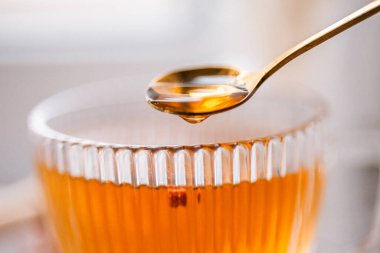 a drop of black tea falls from a golden spoon, macro, close-up view, golden tea, stem composition