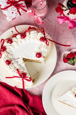 Beyaz bir tabakta beyaz kremalı kalp şeklinde tiramisu pastası, kokteyl kirazı, kırmızı kurdele, Sevgililer Günü pastası, vişneli tiramisu, kremalı pasta, doğum günü tatlıları.