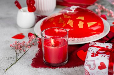 Cam şamdandaki kırmızı mum, kırmızı ve pembe karanfiller, güller, vazodaki çingene, Sevgililer Günü pastası, doğum günü pastası, ışık arka planı, tatil dekorasyonu.