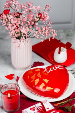 Beyaz bir tabakta altın desenli kırmızı bir kremalı pasta, kırmızı ve pembe karanfiller, güller, vazoda çingene, Sevgililer Günü pastası, doğum günü, aydınlık arka plan, yemek fotoğrafı.