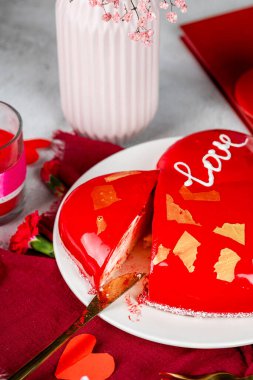 Beyaz bir tabakta altın desenli kırmızı bir kremalı pasta, kırmızı ve pembe karanfiller, güller, vazoda çingene, Sevgililer Günü pastası, doğum günü, aydınlık arka plan, yemek fotoğrafı.