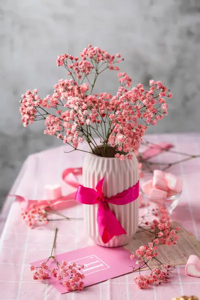 Bir şenlik masasında pembe seramik vazoda bir buket pembe çigila, doğum günü, Sevgililer Günü, masada pembe masa örtüsü, şekerlemeler, kurdeleler, hafif arka plan, durgun hayat, hazırlık.