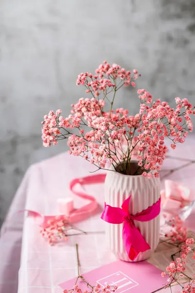 Bir şenlik masasında pembe seramik vazoda bir buket pembe çigila, doğum günü, Sevgililer Günü, masada pembe masa örtüsü, şekerlemeler, kurdeleler, hafif arka plan, durgun hayat, hazırlık.
