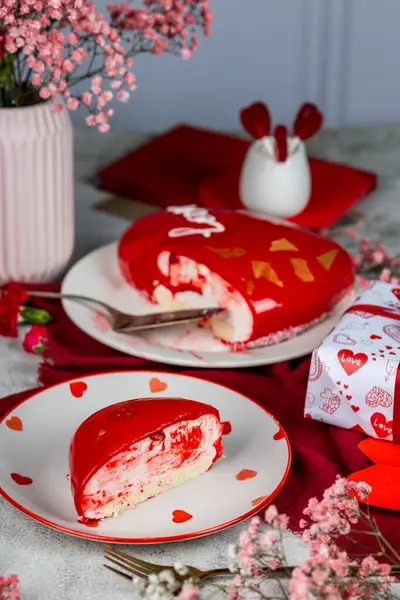 Beyaz bir tabakta altın desenli kırmızı bir kremalı pasta, kırmızı ve pembe karanfiller, güller, vazoda çingene, Sevgililer Günü pastası, doğum günü, aydınlık arka plan, yemek fotoğrafı.