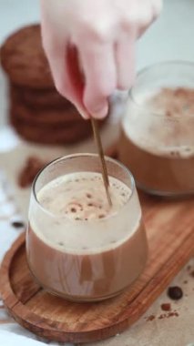 Şeffaf bir fincanda kapuçino yapmak, altın kaşıkla kahve karıştırmak, köpüklü kahve, çikolatalı kurabiye, kahve çekirdekleri, sıcak kompozisyon, köpüklü sabah kahvesi, mochachino