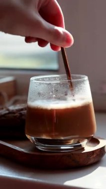 Şeffaf bir fincanda kapuçino yapmak, altın kaşıkla kahve karıştırmak, köpüklü kahve, çikolatalı kurabiye, kahve çekirdekleri, sıcak kompozisyon, köpüklü sabah kahvesi, mochachino