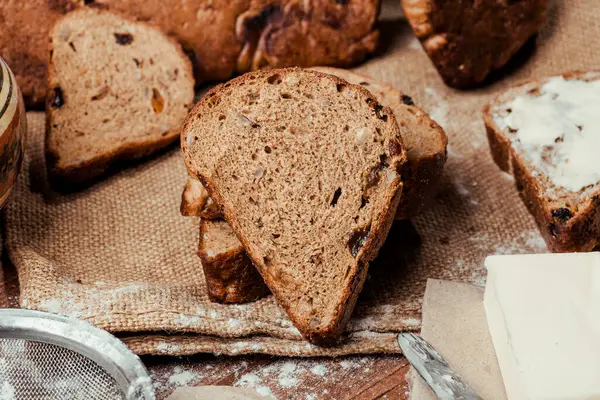 rye bread with raisins, dried apricots, sunflower seeds, caraway seeds, two loaves of bread on a wooden background, flour, sieve, rolling pin, eggs, homemade bread, wheat ears, black bread with butter