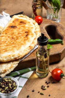 calzone with salami, ham, cheese, tomato, basil, mushrooms, cream sauce on a wooden background, Italian pastries, traditional Italian cuisine, olive oil with spices, food photo, flatlay