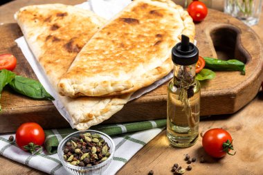 calzone with salami, ham, cheese, tomato, basil, mushrooms, cream sauce on a wooden background, Italian pastries, traditional Italian cuisine, olive oil with spices, food photo, flatlay
