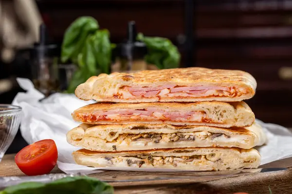 calzone with salami, ham, cheese, tomato, basil, mushrooms, cream sauce on a wooden background, Italian pastries, traditional Italian cuisine, olive oil with spices, food photo, flatlay