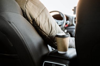 Geri dönüşümlü bir kahve fincanı ve kapağı arabanın arka koltuğundaki şoförün yanındaki koltukta. Arabada kahve var. Arabada güneş ışınları var. Kahve ve çayla arabaya binmek..