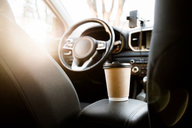 Geri dönüşümlü bir kahve fincanı ve kapağı arabanın arka koltuğundaki şoförün yanındaki koltukta. Arabada kahve var. Arabada güneş ışınları var. Kahve ve çayla arabaya binmek..