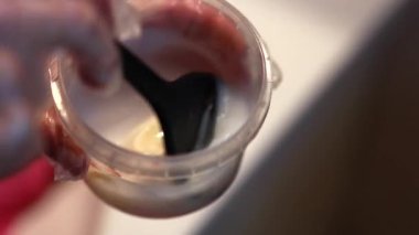 Bir kadın saçını evde boyar. Şeffaf eldivenli bir kadın özel bir fırçayla saç boyasını karıştırıyor..