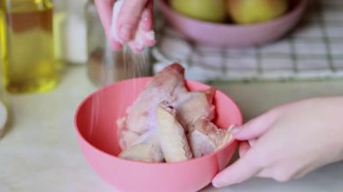 Tavuk kanadı terbiye eden kadın. Tavuk kanatlarını tuz ve karabiberle marine etmek. Mutfak masasının yüzeyine baharatla et sürterek..