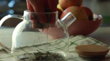 Temiz cam çaydanlıkta bitki çayı hazırlıyorum. Yeşil yapraklı bitkisel çaydanlık, kontrol edilmiş bir kumaşın üzerinde dinleniyor..