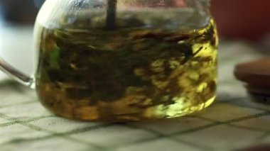 Temiz cam çaydanlıkta bitki çayı hazırlıyorum. Yeşil yapraklı bitkisel çaydanlık, kontrol edilmiş bir kumaşın üzerinde dinleniyor..