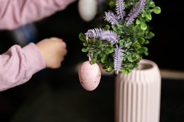 Çocuk, boyalı Paskalya yumurtalarıyla bir dalı süslüyor, bir çocukla Paskalya için hazırlanıyor, dekoratif bir yuvada pembe ve sarı bıldırcın ve tavuk yumurtası boyuyor.