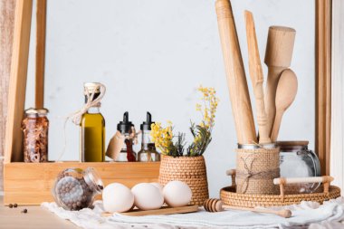 Ahşap mutfak envanteriyle dokuma kabında sade bir hayat, yumurta, yağ ve küçük bir kavanoz biber.