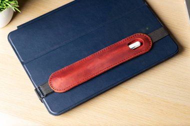 Bir stil için el yapımı kırmızı deri çanta mavi bir çantada bir tablette yatıyor. Stylus ve tablet açık tahta bir masaüstünde. İş konsepti, eğlence, internette sörf.