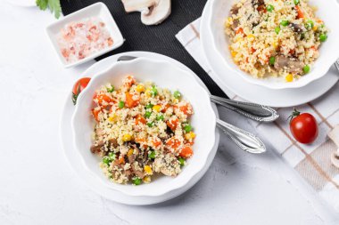 Kuskus, buğday tanelerinden (irmik ya da darı) yapılan bir yemektir. Mantarlı kuskus, mısır, bezelye, şifalı ot, domates. Yan görüş. Flatlay. Hafif arka planda kuskus. Beyaz tabakta kuskus.