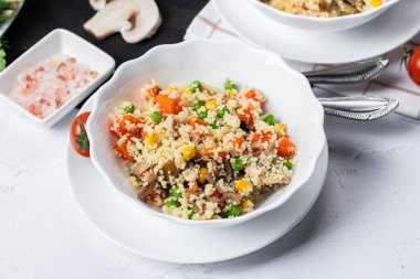 Kuskus, buğday tanelerinden (irmik ya da darı) yapılan bir yemektir. Mantarlı kuskus, mısır, bezelye, şifalı ot, domates. Yan görüş. Flatlay. Hafif arka planda kuskus. Beyaz tabakta kuskus.