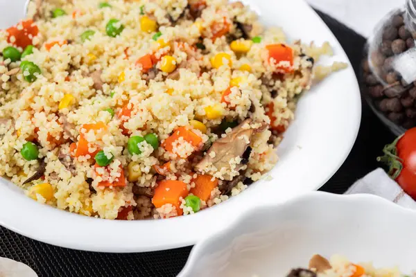 Kuskus, buğday tanelerinden (irmik ya da darı) yapılan bir yemektir. Mantarlı kuskus, mısır, bezelye, şifalı ot, domates. Yan görüş. Flatlay. Hafif arka planda kuskus. Beyaz tabakta kuskus.