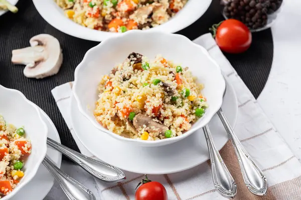 Kuskus, buğday tanelerinden (irmik ya da darı) yapılan bir yemektir. Mantarlı kuskus, mısır, bezelye, şifalı ot, domates. Yan görüş. Flatlay. Hafif arka planda kuskus. Beyaz tabakta kuskus.