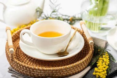 Beyaz porselen fincanlar ve çaydanlıkta yeşil çay, cam vazoda laleler, mimoza çiçekleri, açık arkaplan. Çay partisi..