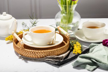 Beyaz porselen fincanlar ve çaydanlıkta yeşil çay, cam vazoda laleler, mimoza çiçekleri, açık arkaplan. Çay partisi..