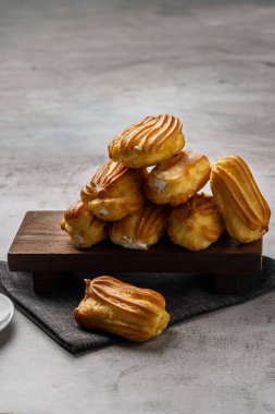 Kremalı Fransız ekini. Beyaz tabakta kremalı profiterol. Yan görüş. Kremalı ev yapımı hamur işleri. Gri arka plan. Kahveli profiterol..
