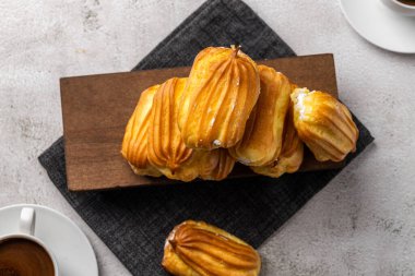 Kremalı Fransız ekini. Beyaz tabakta kremalı profiterol. Yan görüş. Kremalı ev yapımı hamur işleri. Gri arka plan. Kahveli profiterol..