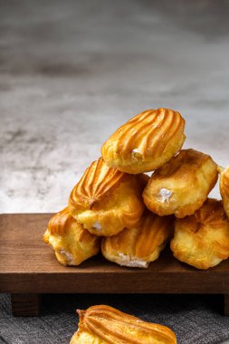 Kremalı Fransız ekini. Beyaz tabakta kremalı profiterol. Yan görüş. Kremalı ev yapımı hamur işleri. Gri arka plan. Kahveli profiterol..