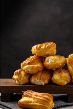 Kremalı Fransız ekini. Beyaz tabakta kremalı profiterol. Yan görüş. Kremalı ev yapımı hamur işleri. Karanlık arka plan. Kahveli profiterol..