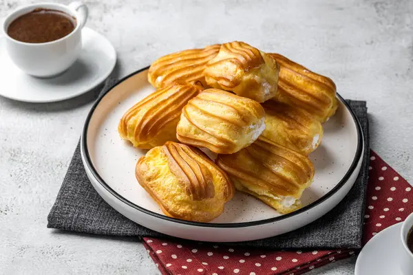 Kremalı Fransız ekini. Beyaz tabakta kremalı profiterol. Üst Manzara. Kremalı ev yapımı hamur işleri. Gri arka plan. Kahveli profiterol..