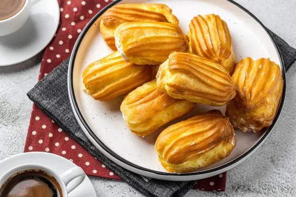 Kremalı Fransız ekini. Beyaz tabakta kremalı profiterol. Üst Manzara. Kremalı ev yapımı hamur işleri. Gri arka plan. Kahveli profiterol..