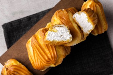 Kremalı Fransız ekini. Beyaz bir tabakta kremalı profiteroller, krem görünür. Kremalı ev yapımı hamur işleri..