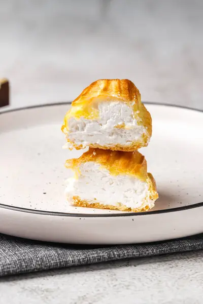 Kremalı Fransız ekini. Beyaz bir tabakta kremalı profiteroller, krem görünür. Kremalı ev yapımı hamur işleri..