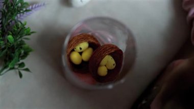 Çocuk, boyalı Paskalya yumurtalarıyla bir dalı süslüyor, bir çocukla Paskalya için hazırlanıyor, dekoratif bir yuvada pembe ve sarı bıldırcın ve tavuk yumurtası boyuyor.