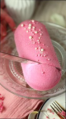 Bıçak, kremalı keki pembe kadife, mango köpüğü ve tutku meyvesi ile cam bir pasta tabağında keser..
