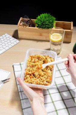Ofis ortamı, yemek molası. İş yerinde atıştırmalık bir şeyler. Çizgili bir kumaşa konulmuş havuçlu ve tavuklu kızarmış pirinç konteynırı. Plastik çatal tutan bir el. Limonlu bir bardak su..