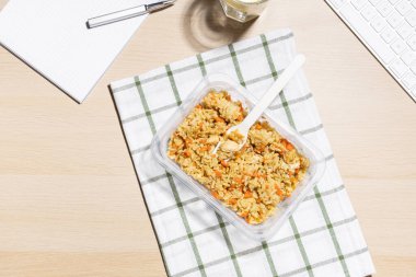 Ofis ortamı, yemek molası. İş yerinde atıştırmalık bir şeyler. Çizgili bir kumaşa konulmuş havuçlu ve tavuklu kızarmış pirinç konteynırı. Limonlu bir bardak su. Yakın klavye