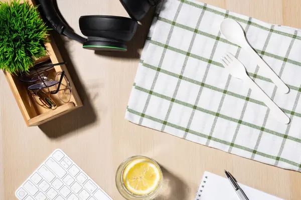 Ofisteki işyerinde atıştırmalık. İyi düzenlenmiş bir çalışma alanında bir klavye, yeşil aksanlı kulaklıklar ve tahta bir masanın üzerinde kontrol edilmiş bir peçete bulunur. Plastik kaşık ve çatal..