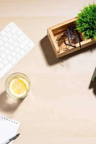 Su dolu berrak bir bardak ve ahşap bir masada limon dilimi. Yakınlarda, beyaz bir bilgisayar tuş tahtası. Ofis ortamı, dinlendirici bir mola ya da iş sırasında susuz kalma girişiminde bulunulduğunu gösteriyor.