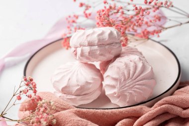 Pembe böğürtlen şekerlemesi beyaz tabakta, arka planda pembe kurdele ve çiçeklerin yanında. Elma sosu ve yumurta beyazından yapılmış beyaz ve pembe zefyr. Düşük kalorili tatlılar. Vegan şekerlemesi..