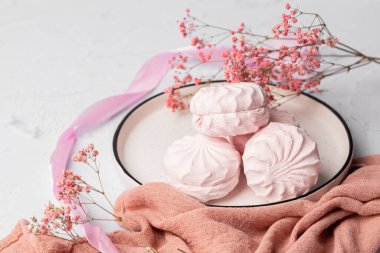 Pembe böğürtlen şekerlemesi beyaz tabakta, arka planda pembe kurdele ve çiçeklerin yanında. Elma sosu ve yumurta beyazından yapılmış beyaz ve pembe zefyr. Düşük kalorili tatlılar. Vegan şekerlemesi..