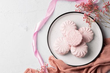 Pembe böğürtlen şekerlemesi beyaz tabakta, arka planda pembe kurdele ve çiçeklerin yanında. Elma sosu ve yumurta beyazından yapılmış beyaz ve pembe zefyr. Düşük kalorili tatlılar. Vegan şekerlemesi..